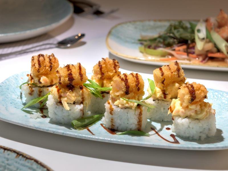 Gegrilde garnalen sushirollen geserveerd op een rechthoekig wit bord met garnering.