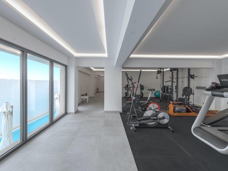 Moderne sportschool met cardioapparaten naast grote ramen en een trap naar een balkon.