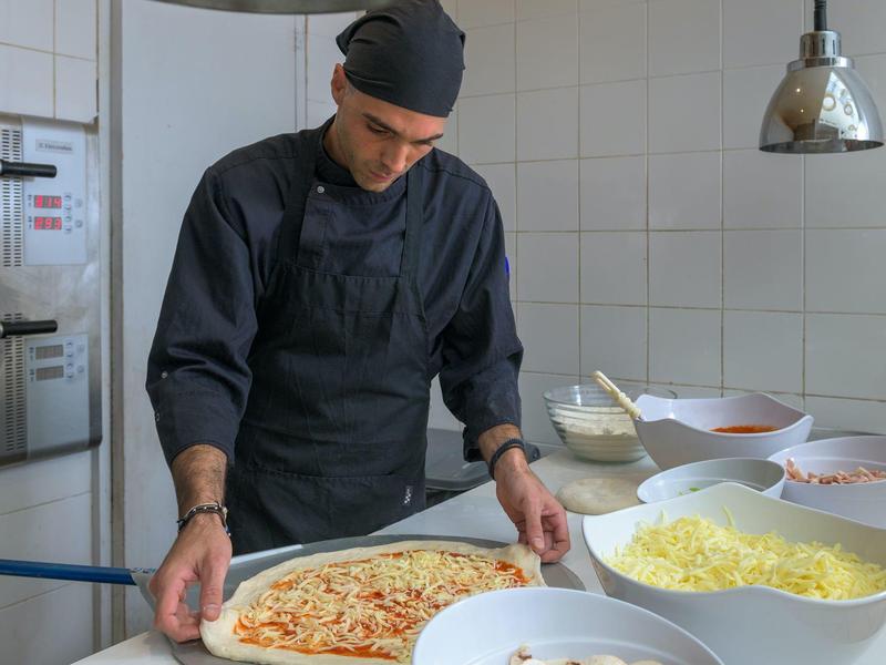 Chef bereidt zorgvuldig een pizza in een keuken met kommen kaas en saus.