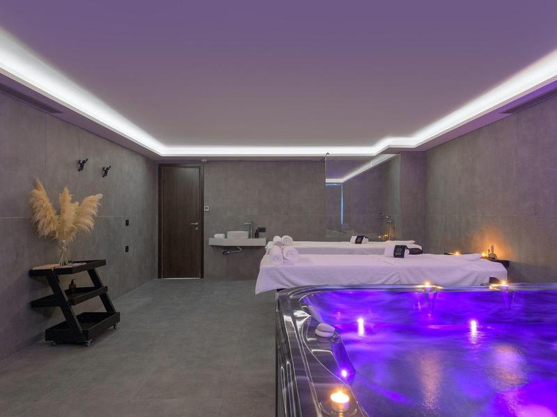 Luxe spa kamer met massagetafels, gedimd licht en een gloeiende paarse jacuzzi.