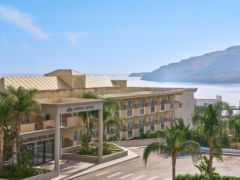 Modern hotelgebouw bij de zee met palmbomen en bergen op de achtergrond.