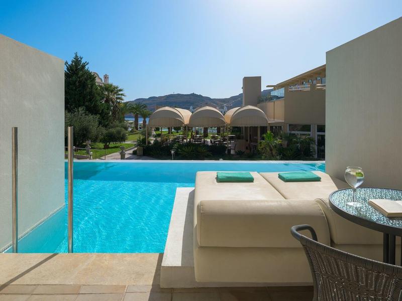 Uitzicht vanaf het zwembad met ligbedden, tafel en helderblauw water onder zonnige lucht.