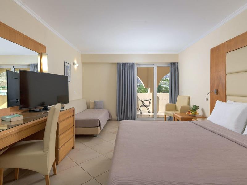 Moderne hotelkamer met tweepersoonsbed, bureau, tv, bank en balkon met zitje.