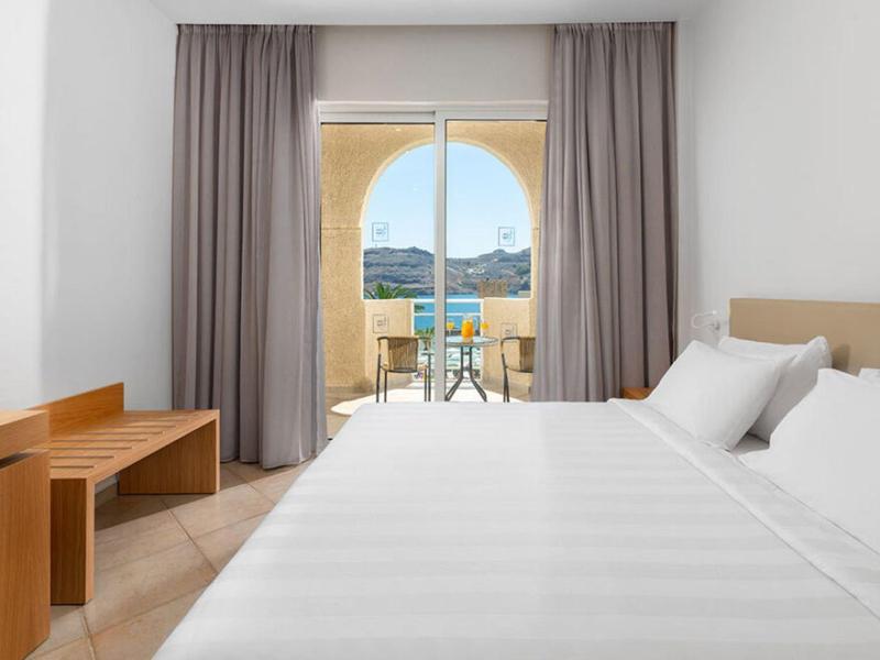 Lichte hotelkamer met groot bed, bureau en uitzicht op balkon en berglandschap.