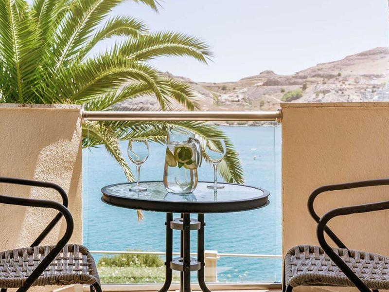Twee stoelen en een tafel met bloemen met uitzicht op zee en palmbomen.