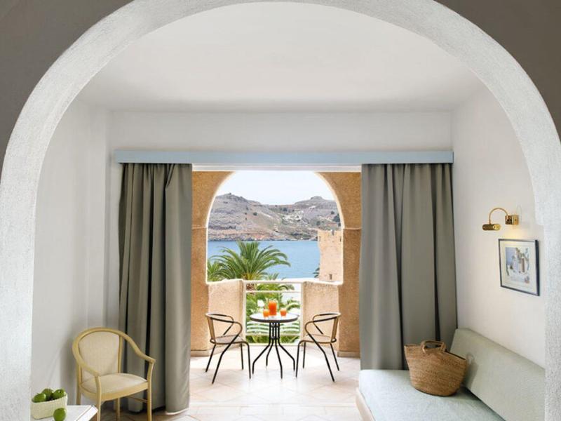 Uitzicht door een boog naar een balkon met tafel en stoelen met uitzicht op bergen en zee.