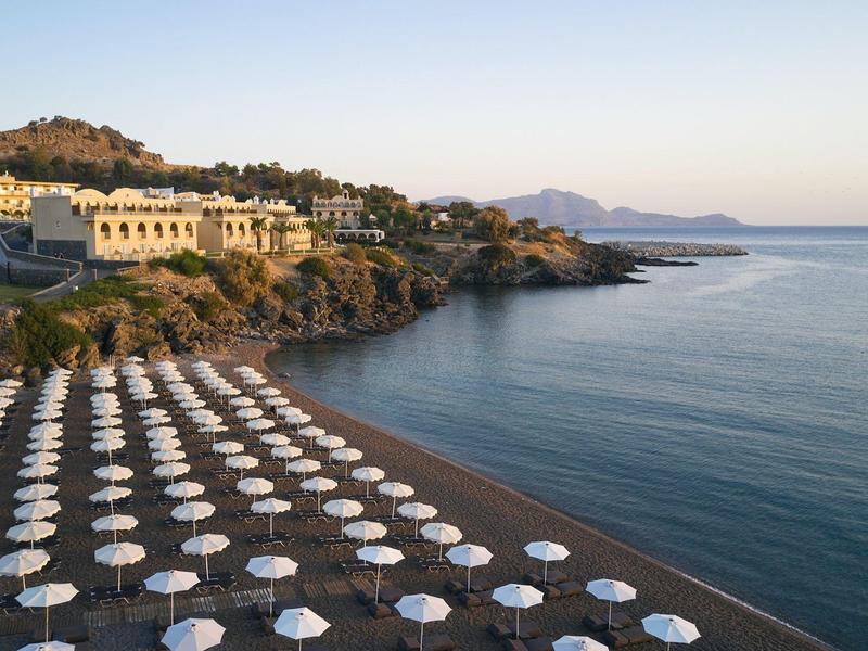 Strand met witte parasols voor een hotel bij een rustige baai bij zonsondergang.