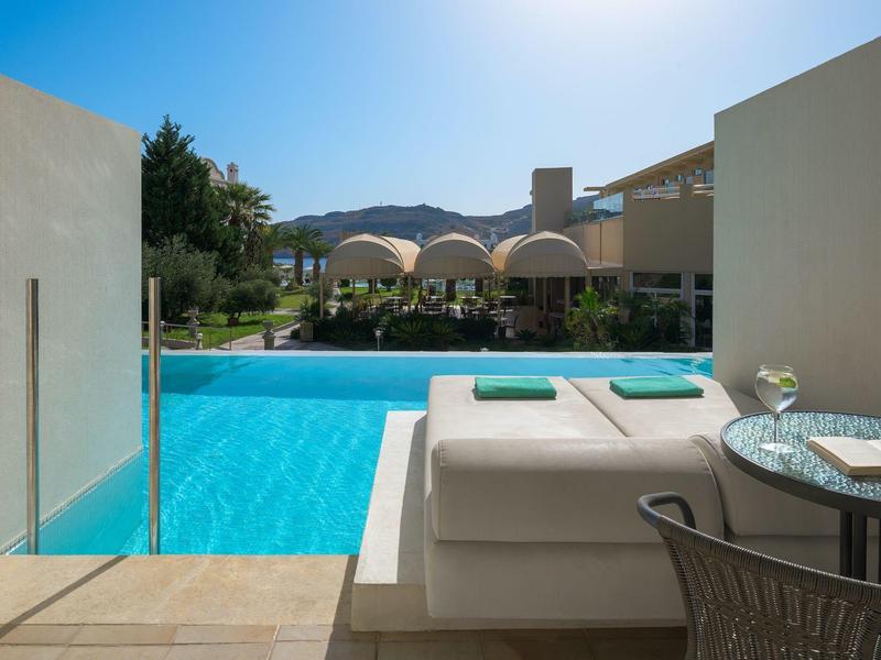 Moderne zwembadomgeving met ligstoelen en gebogen hotelgebouwen onder een blauwe lucht.