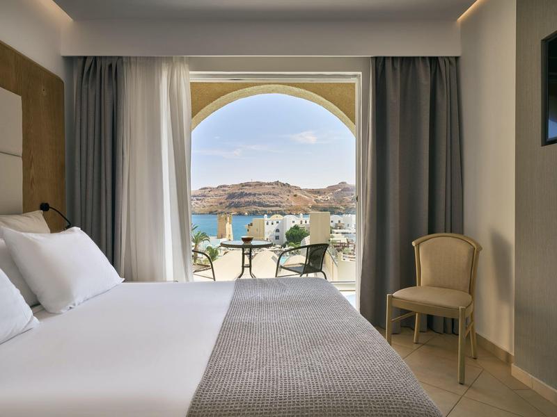 Modern hotelkamer met tweepersoonsbed en uitzicht op terras en zee door groot raam.