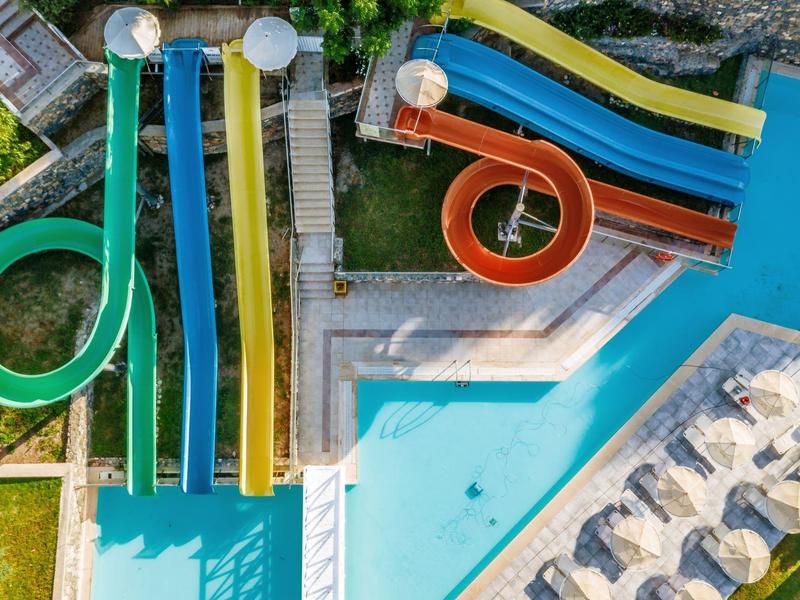 Buitenwaterpark met meerdere kleurrijke glijbanen en een zwembad omringd door ligstoelen.