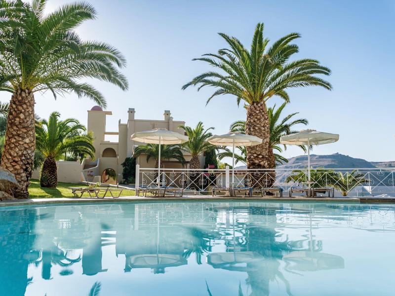 Resortzwembad met palmbomen en bergzicht onder een heldere blauwe lucht.
