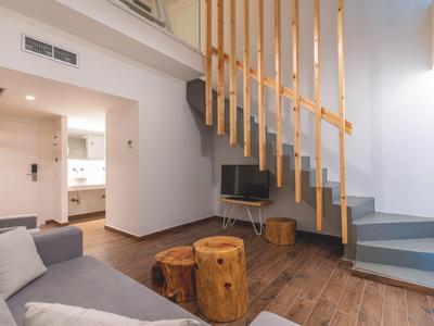 Wohnzimmer mit grauem Sofa, Holzstämmen als Hocker, Holztreppe und Flachbildschirm-TV.