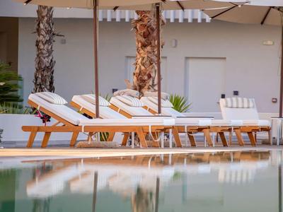 Ruhebereich mit Liegestühlen und Sonnenschirmen neben einem klaren Pool, Palmen im Hintergrund.