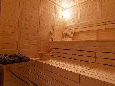 Sauna innen mit hellen Holzpaneelen, mehrstufigen Bänken und Saunaofen mit Steinen.