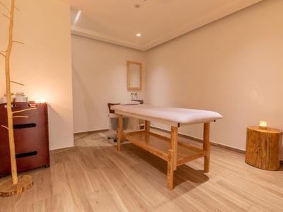 Einfach eingerichteter Wellnessraum mit Massageliege, hellem Holzboden und minimaler Dekoration.