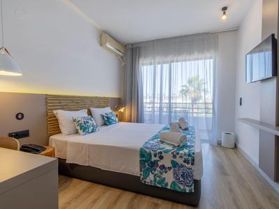 Helles Schlafzimmer mit Doppelbett, floralem Bettbezug, Fernseher, großem Fenster und Holzboden.
