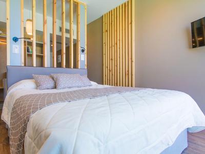 Helles Schlafzimmer mit großem Bett, hellen Bettdecken, Holzwand und Wand-TV.