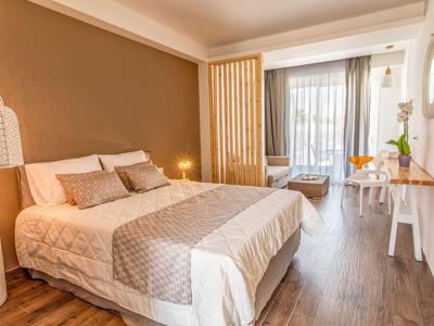 Helles Schlafzimmer mit großem Bett, Holzfußboden, Vorhängen und Balkon mit Sicht auf draußen.