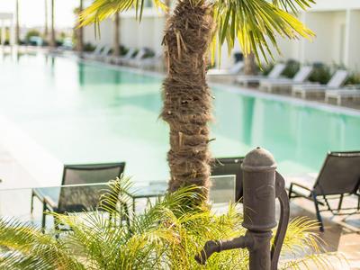 Schwimmbad mit Palmen, Stühlen und einem alten Wasserpumpenbrunnen im Vordergrund.