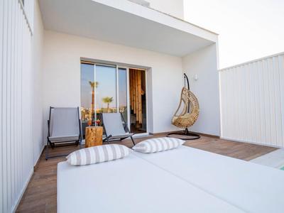 Moderner Balkon mit Holzboden, Hängesessel, Liegestühlen und Blick auf Palmen.