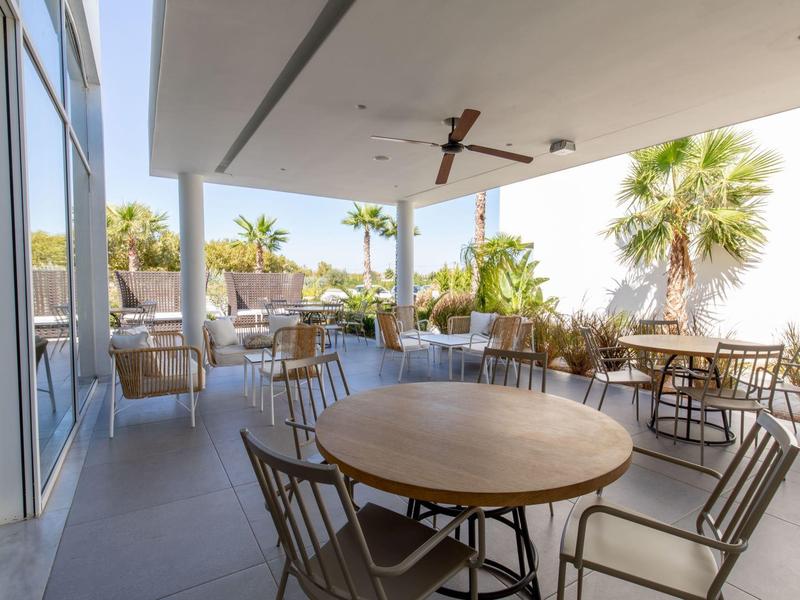 Taras hotelowy z stolikami i krzesłami, widok na palmy i czyste niebo.