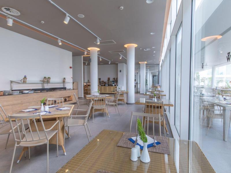 Jasna restauracja z drewnianymi meblami i dużymi oknami wpuszczającymi światło dzienne.