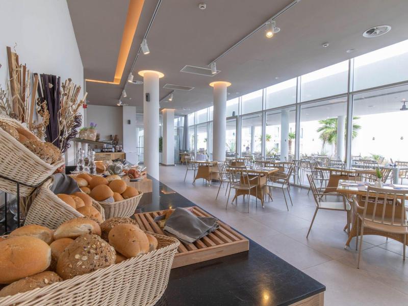 Jasna sala śniadaniowa z koszem świeżych bułek i drewnianymi oraz szklanymi siedzeniami.