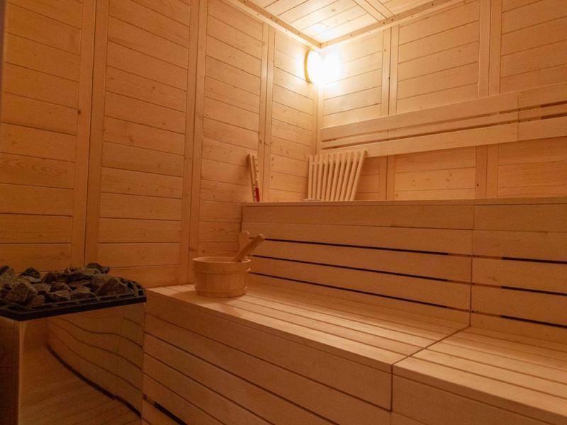 Jasna sauna z drewnianymi ławkami wielopoziomowymi i piecem z kamieniami.