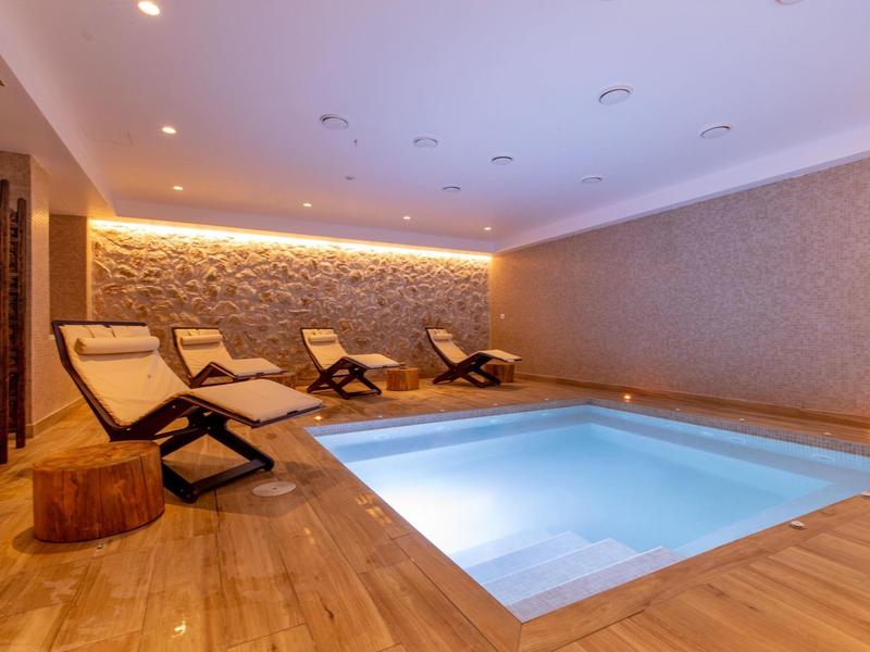 Basen wewnętrzny z leżakami i ciepłą drewnianą podłogą w przytulnym pokoju spa.