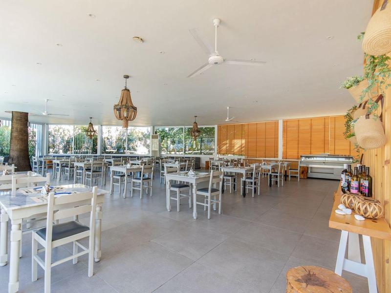 Jasna, otwarta jadalnia z szarymi krzesłami, stołami, roślinami i huśtawkami.