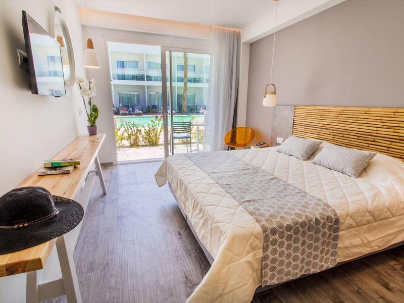 Jasny pokój hotelowy z podwójnym łóżkiem, drewnianymi akcentami i tarasem z widokiem na basen.