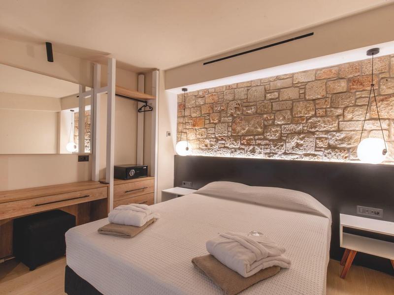 Przytulny pokój hotelowy z łóżkiem podwójnym, stolikami nocnymi i oświetloną ścianą z kamienia.