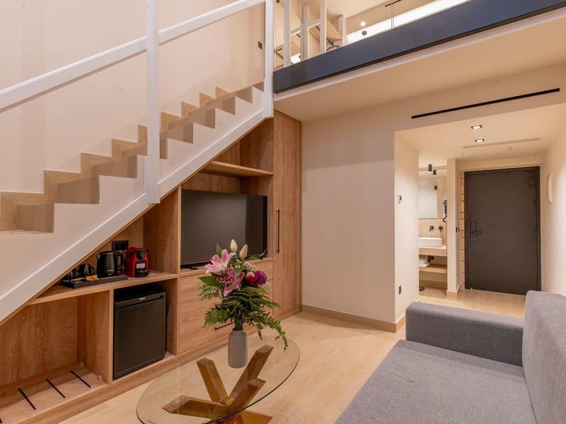 Nowoczesna część pokoju hotelowego ze schodami, telewizorem, sofą i kwiatową dekoracją.