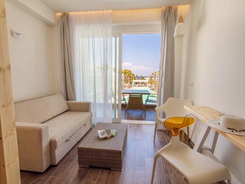 Jasny salon z kanapą, stołem do masażu i widokiem na balkon z widokiem na morze.