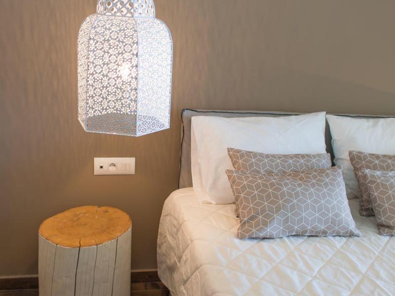 Nowoczesny pokój hotelowy z łóżkiem, poduszkami, stolikiem nocnym i dekoracyjną lampą wiszącą.