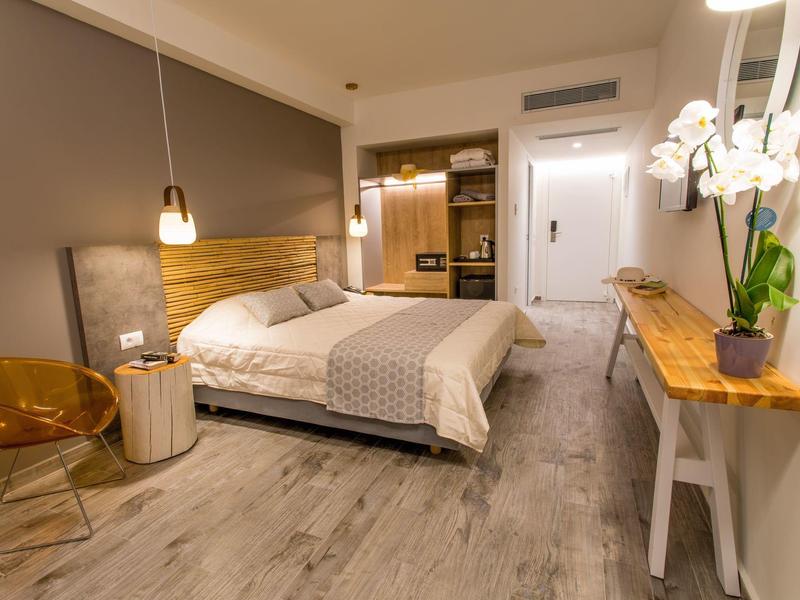 Nowoczesny pokój hotelowy z łóżkiem podwójnym, drewnianymi akcentami i roślinami dekoracyjnymi.