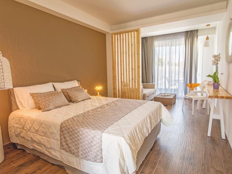 Nowoczesna sypialnia z dużym łóżkiem, ciepłymi kolorami i balkonem z miejscami do siedzenia.