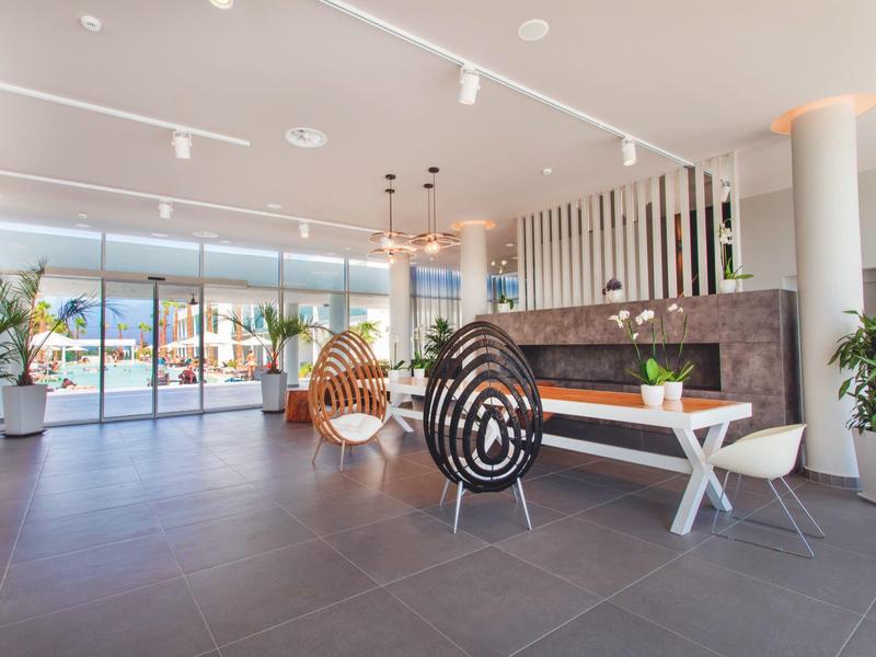 Nowoczesna recepcja hotelowa z eleganckimi miejscami do siedzenia, roślinami i dużym oknem na taras.