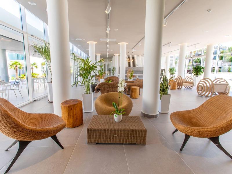 Jasny hol hotelowy z nowoczesnymi, okrągłymi fotelami i dużymi oknami z widokiem na palmy.