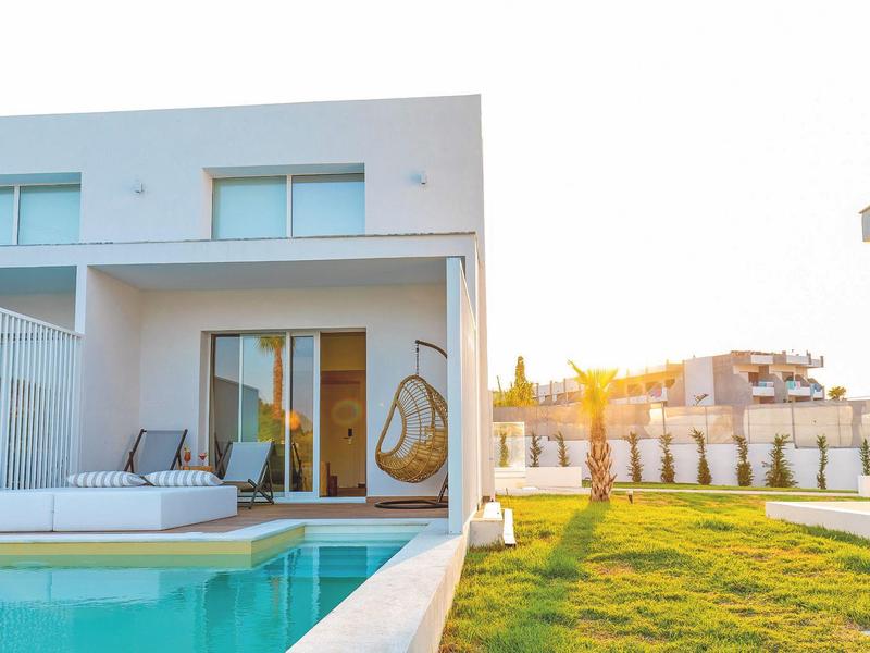 Nowoczesny biały domek wakacyjny z basenem i ogrodem o zachodzie słońca.