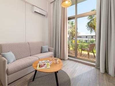 Gezellige hotelkamer met bank, koffietafel en balkon met uitzicht op palmbomen.