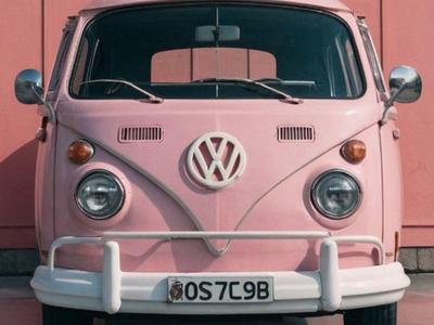 Vooraanzicht van een vintage roze Volkswagen busje geparkeerd bij een roze muur.