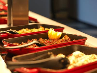 Verschillende warme gerechten in rode serveerschalen op een buffet.