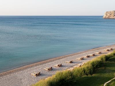 Strand met ligstoelen langs rustige kust en heldere lucht.