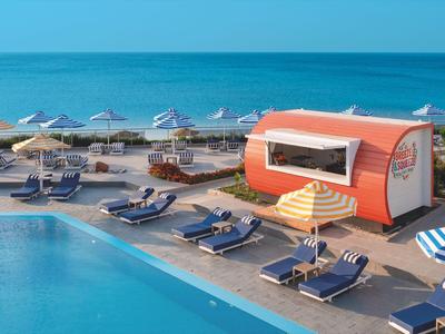 Bar sulla spiaggia e lettini accanto a una piscina con vista sul mare.