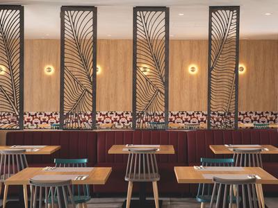 Area lounge moderna in hotel con pareti in legno, divisori geometrici e posti a sedere con tavoli e sedie.