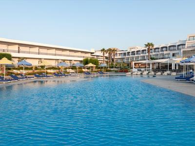 Grande piscina blu davanti a un hotel moderno con ombrelloni e lettini.
