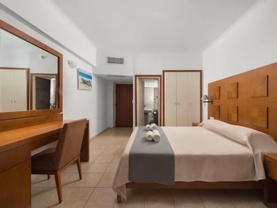 Moderne hotelkamer met tweepersoonsbed, bureau, stoel en grote spiegels in neutrale tinten.