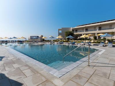 Moderner Hotelpool mit Liegestühlen und Blick auf das Meer bei strahlendem Himmel.
