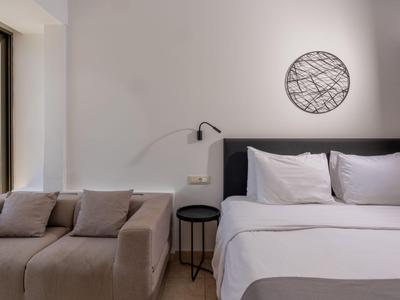 Moderní hotelový pokoj s velkou postelí, pohovkou a minimalistickou nástěnnou dekorací.